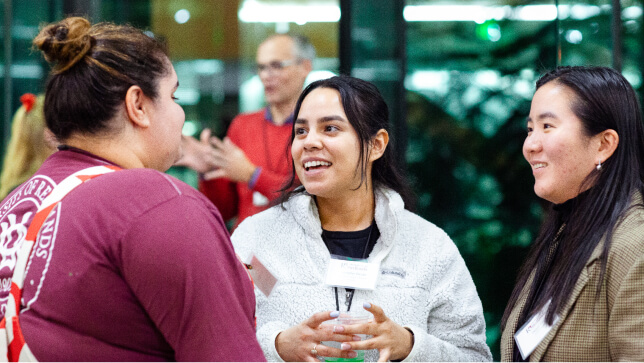 초록색 잎으로 가득한 유리로 된 밝은 로비에서 캐주얼한 차림으로 출입증을 목에 걸고 대화 중인 사람들