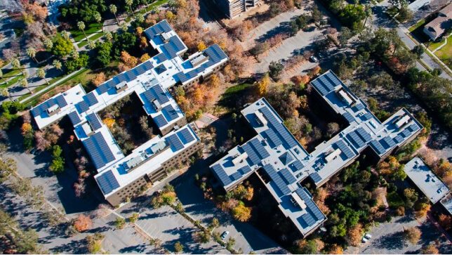 태양광 패널이 옥상을 뒤덮고 야자수가 흩어져 있는 언덕에 위치한 대형 오피스 단지의 조감도